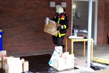 Unter Atemschutz trägt ein Feuerwehrmann Putzmittel ins Freie. Foto: FF Halstenbek